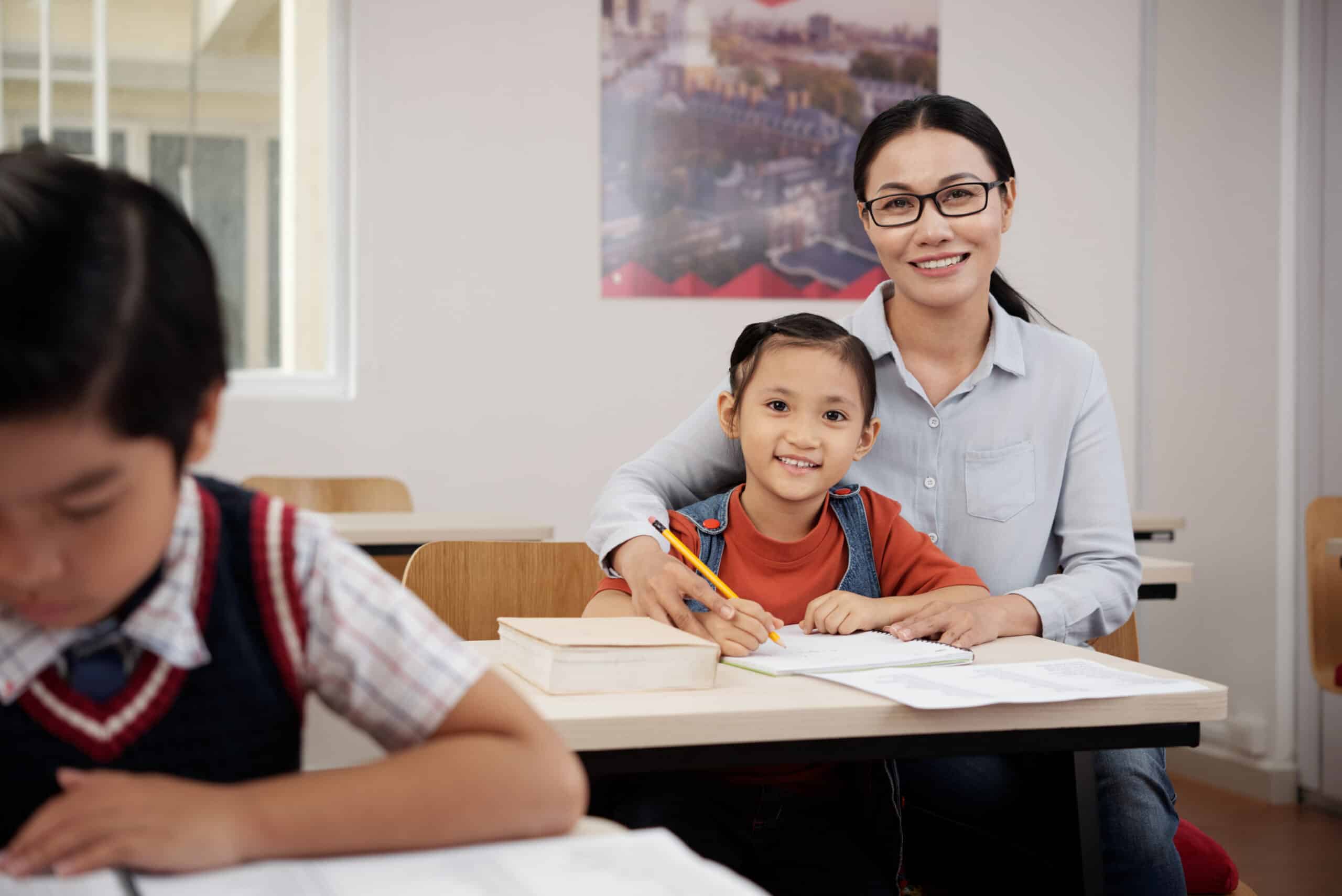 Teacher helping student Cheerful Vietnamese teacher helping little girl with difficult task